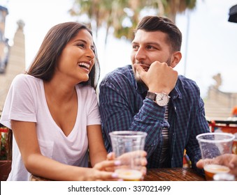 attractive hispanic couple drinking beer and having fun at outdoor restaurant