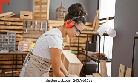 Attractive hispanic female carpenter smiling at her carpentry workshop, young, beautiful woman with curly hair, glasses and headphones bringing joy to the woodworking industry - Powered by Shutterstock