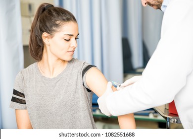 Attractive Hispanic Female Patient Getting Vaccine On Her Arm By A Doctor In Hospital