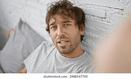 Attractive hispanic man with beard and green eyes taking a selfie in a cozy indoor bedroom environment. - Powered by Shutterstock