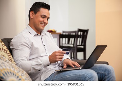 Attractive Hispanic Man Using His Credit Card And Laptop To Book A Trip Online