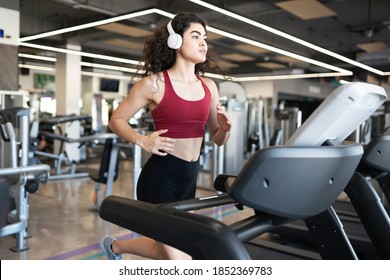 Attractive Hispanic Woman Running Fast On The Treadmill While Listening To Music At A Fitness Center