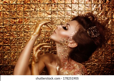 Attractive hot brunette with beautiful golden makeup and gold caramel painted hands is posing in front of abstract golden background