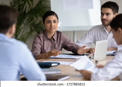 Attractive indian ethnic businesswoman with businessman partner talking in boardroom at meeting. Young confidence woman with male assistant training diverse corporate team at briefing.