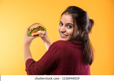 Attractive Indian/Asian Girl Eating Burger On White Or Yellow Background
