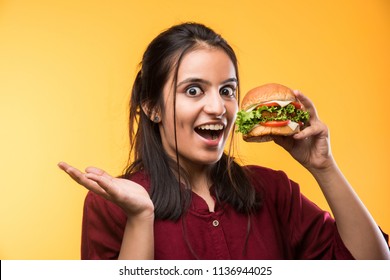 Attractive Indian/Asian Girl Eating Burger On White Or Yellow Background
