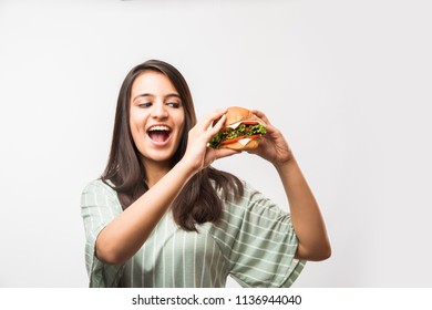 Attractive Indian/Asian Girl Eating Burger On White Or Yellow Background
