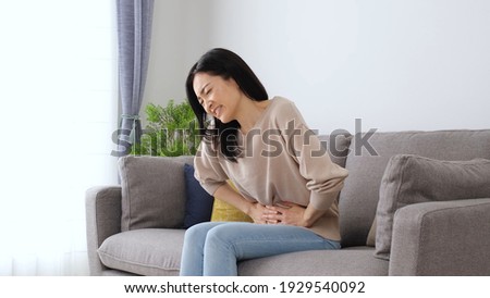 attractive japanese woman with stomach ache sitting sofa in the living room