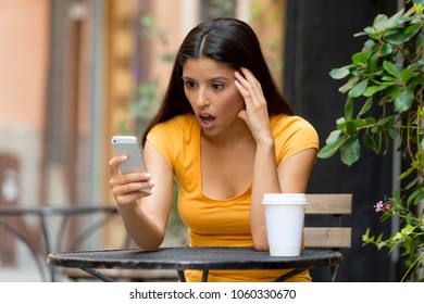 Attractive Latin Woman In Her Twenties Shocked While Reading A Tex Message On Her Smart Phone At A Coffeeshop