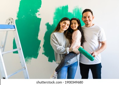 Attractive Latin Woman And Man Posing Happily With Her Daughter While Painting And Remodeling The Bedroom. Happy Family Redecorating Their Home 