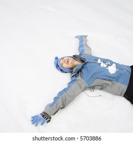 Attractive Laughing Mid Adult Caucasian Woman Wearing Blue Ski Clothing Lying In Snow Making Snow Angel.