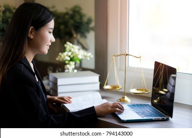 Attractive Lawyer Woman Typing On Computer With Law Textbooks And Scale Of Justice On Table At Law Firm. Work On Advice Document For Defendant In Courtroom. 