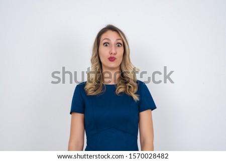 Attractive light haired female rounds lips, wears casual clothes, looks directly into camera, expresses her satisfaction, isolated over gray background. People, body language concept.