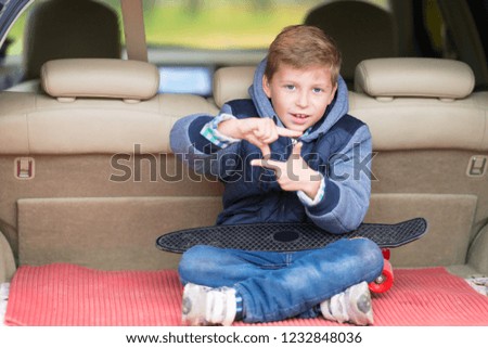 Attractive little boy sitting in the trunk of a car making a frame gesture with his fingers as he smiles at the camera