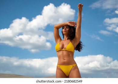 Attractive long hair woman in yellow bikini posing with one arm raised 