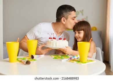 Attractive loving father baby celebrating his child birthday, sitting at table with birthday cake and drink, father kissing his daughter, celebrating together, expression love and gentle.