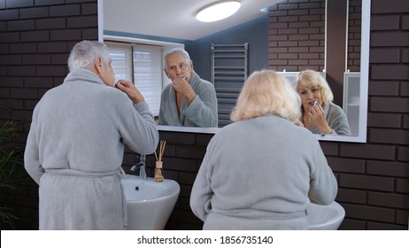 Attractive Loving Old Senior Couple Man And Woman Brushing Teeth And Looking Into A Mirror. Cheerful Elderly Grandmother And Grandfather Doing Morning Hygiene At Luxury Bathroom At Home