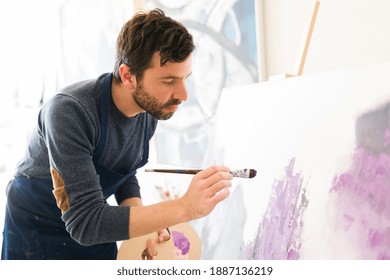 Attractive male artist in his 30s is giving the last touches of paint to the new colorful painting that he is doing on his art studio - Powered by Shutterstock