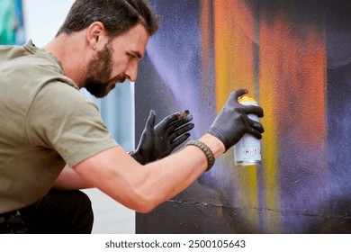 Attractive male artist is painting picture with paint spray can spraying it onto canvas at outdoor street exhibition, side view of man art maker - Powered by Shutterstock