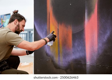 Attractive male artist is painting picture with paint spray can spraying it onto canvas at outdoor street exhibition, side view of man art maker - Powered by Shutterstock