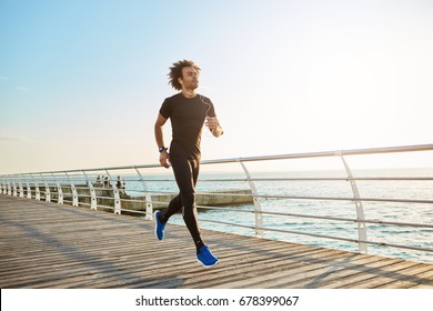 Attractive Male Athlete Wearing Stylish Black Sport Clothing And Blue Sneakers. Figure Of Man Athlete Doing Cardio Running Exercises On Sunny Summer Morning. People, Sports, Fitness And Health Concept