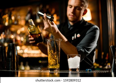 Attractive male bartender pouring a yellow liqour from the jigger to a measuring glass cup on the bar counter