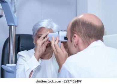 Attractive male ophthalmologist is checking eye vision of middle aged woman in modern clinic, doctors and ophthalmology clinic patients. - Shutterstock ID 2237462499