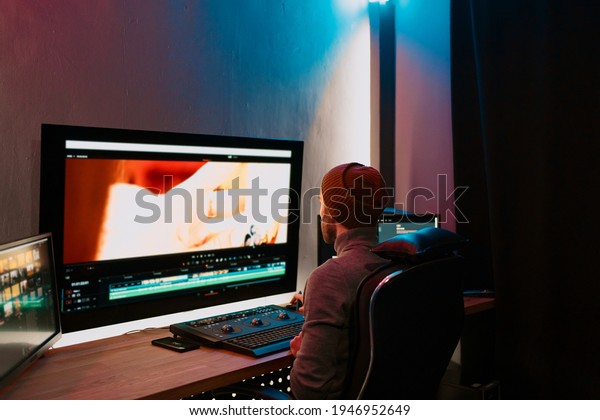 Attractive Male Video Editor Works with Footage or\
Video on His Personal Computer, he Works in Creative Office Studio\
or home. Neon lights