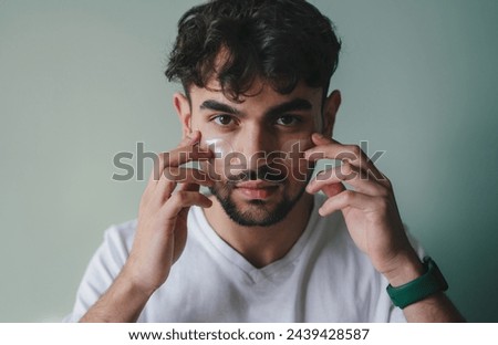 Attractive man applying eye patch facial with collagen looking at camera, isolated over grey background. Male morning daily beauty procedures. Skincare and