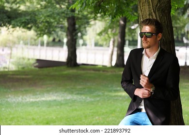 Attractive Man In Blue Jeans And Black Blazer In A Park. 