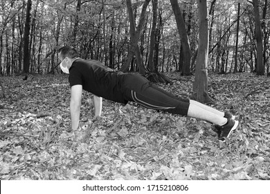 Attractive Man Doing Plank Yoga Pose In Nature And Wearing Face Mask To Protect From Coronavirus