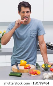 Attractive Man Eating A Slice Of Bell Pepper In The Kitchen