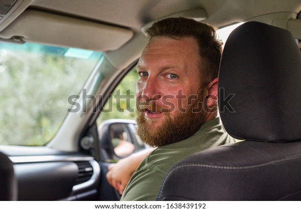 Attractive man in good car. Man with a beard in a\
car. A man with a beard in a car is not driving. The guy is a\
passenger in the car in the front seat. Portrait of a man. Do not\
distract the driver