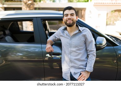 Attractive Man In His 20s Smiling And Making Eye Contact While Standing Next To A Black Car Outside His House