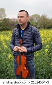 attractive man posing in beautiful big yellow blooming rapeseed or oilseed rape field. boy holding violin. spring nature wallpaper. farming.
