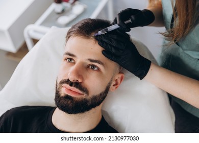 An attractive man receives mesotherapy injections to treat hair loss at the clinic. Injections into the skin and scalp - Shutterstock ID 2130977030