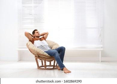 Attractive Man Relaxing In Papasan Chair Near Window At Home. Space For Text