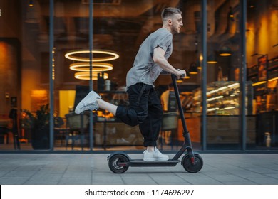 Attractive man riding a kick scooter at cityscape background.