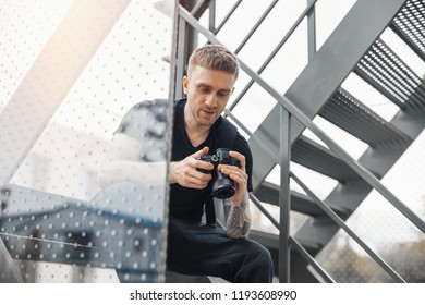 Attractive man sitting at staircase and checking photos in camera. - Powered by Shutterstock