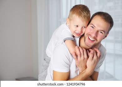 Attractive man smiling and looking at camera while carrying sweet boy on back at home - Shutterstock ID 1241934796