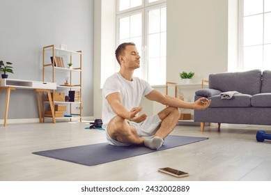 Attractive man in sports outfit doing yoga and meditating on exercise mat. Sporty peaceful calm young man with closed eyes practicing yoga in lotus pose at home. Healthy lifestyle concept - Powered by Shutterstock