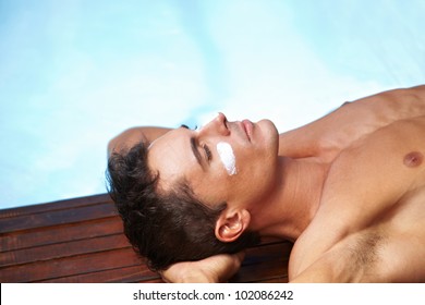 Attractive Man Sunbathing With Sunscreen On His Face Near Pool