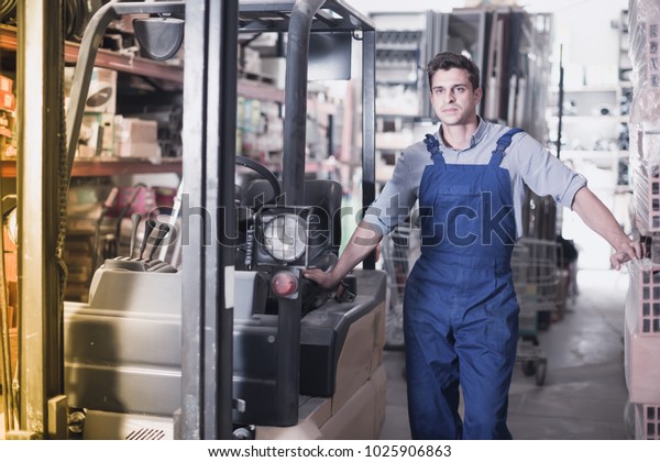 attractive man in unifom is using Ñ�argo\
moving machine in the warehouse building\
store