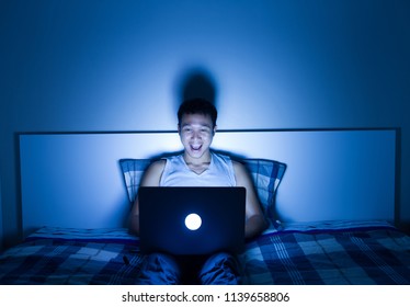 attractive man using laptop computer and reflection from blue light screen to his eyes on bed room at night, hard work