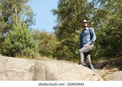 Attractive man wearing a jeans shirt and jeans, standing on top of a mountain looking forward, on a sunny summer day.