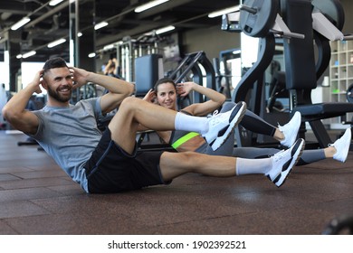 Attractive Man And Woman Working In Pairs Performing Sit Ups In Gym