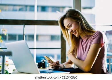 Attractive Manager Sitting In Cafe Interior Checking Email Box On Smartphone Receiving Good Advertising Offer; Cheerful Blonde Student Sharing Multimedia Files On Mobile Synchronize With Laptop