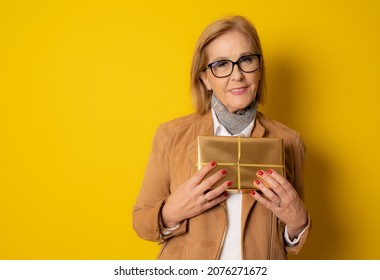 Attractive mature aged aged woman holding presents gift box feels happy studio isolated over yellow background