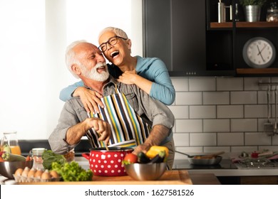 Attractive Mature Couple Is Celebrating Valentine’s Day At House Kitchen. Happy Elderly Concept With Mature Pensioners.