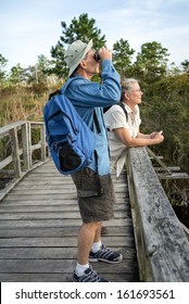Attractive mature couple hiking and birdwatching on old wooden footbridge in Florida wetlands.